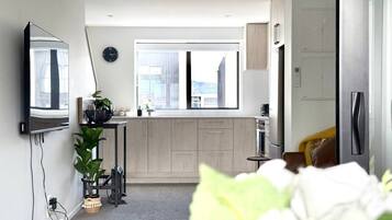 A modern, compact apartment with a kitchenette, a large window, and a flat-screen TV mounted on the wall.