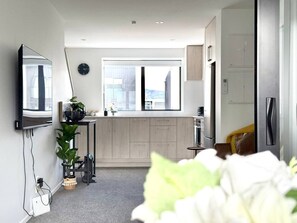 Un apartamento moderno y funcional con kitchenette, un ventanal grande y un televisor de pantalla plana montado en la pared.