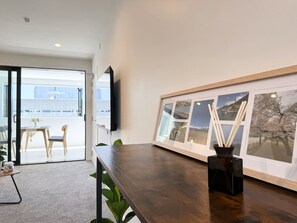 Una habitación moderna con una mesa de madera oscura, una composición de fotografías enmarcadas en la pared y vistas a una zona de estar exterior a través de una puerta de cristal.