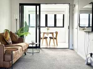 A modern living room with a sofa, a small table, and a dining area with chairs.