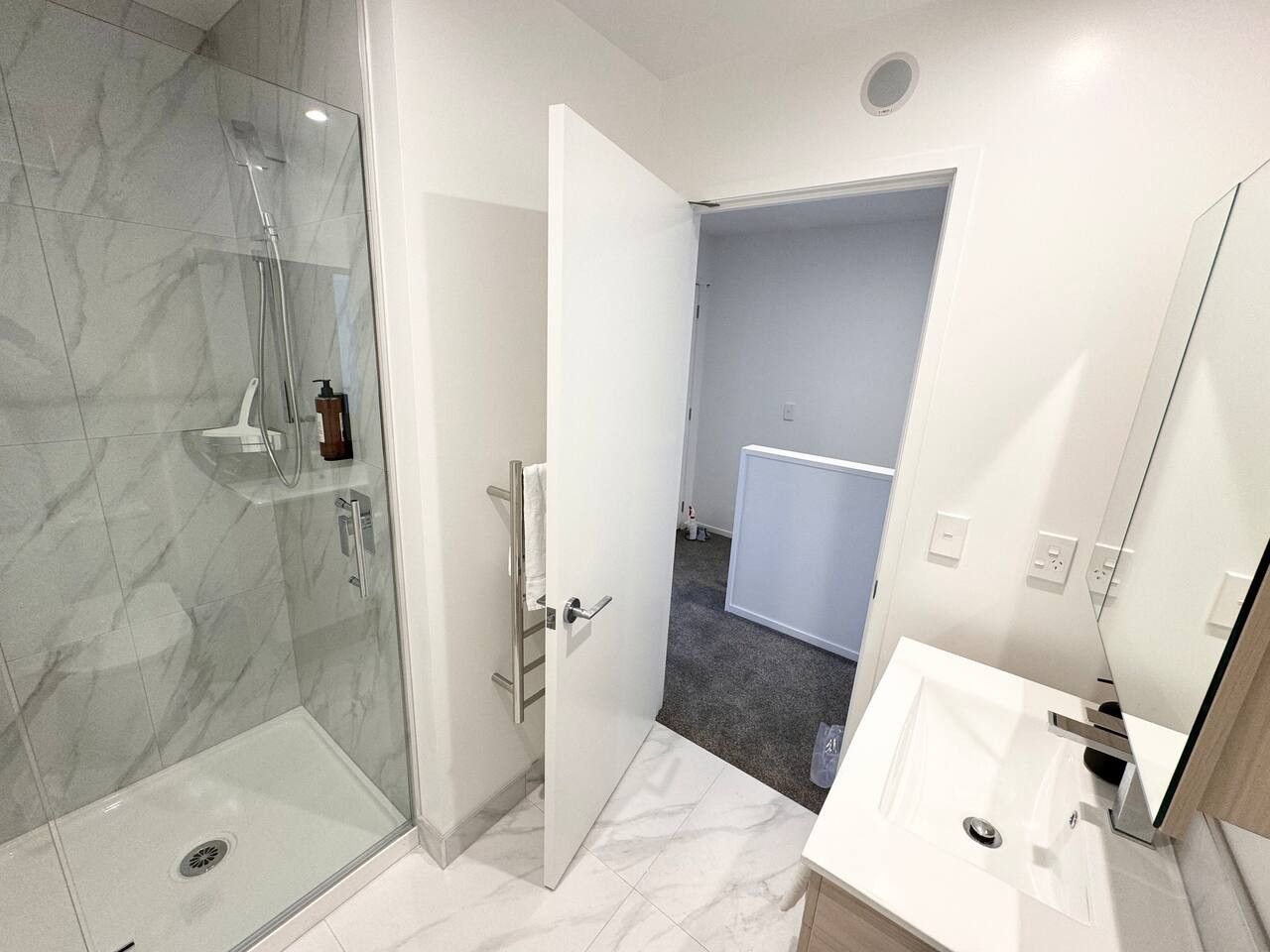 A modern bathroom with a glass shower enclosure, a white sink, and a mirror.
