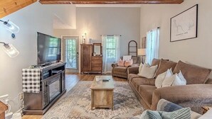 Una sala de estar con televisor, sofá y vigas de madera en el techo.