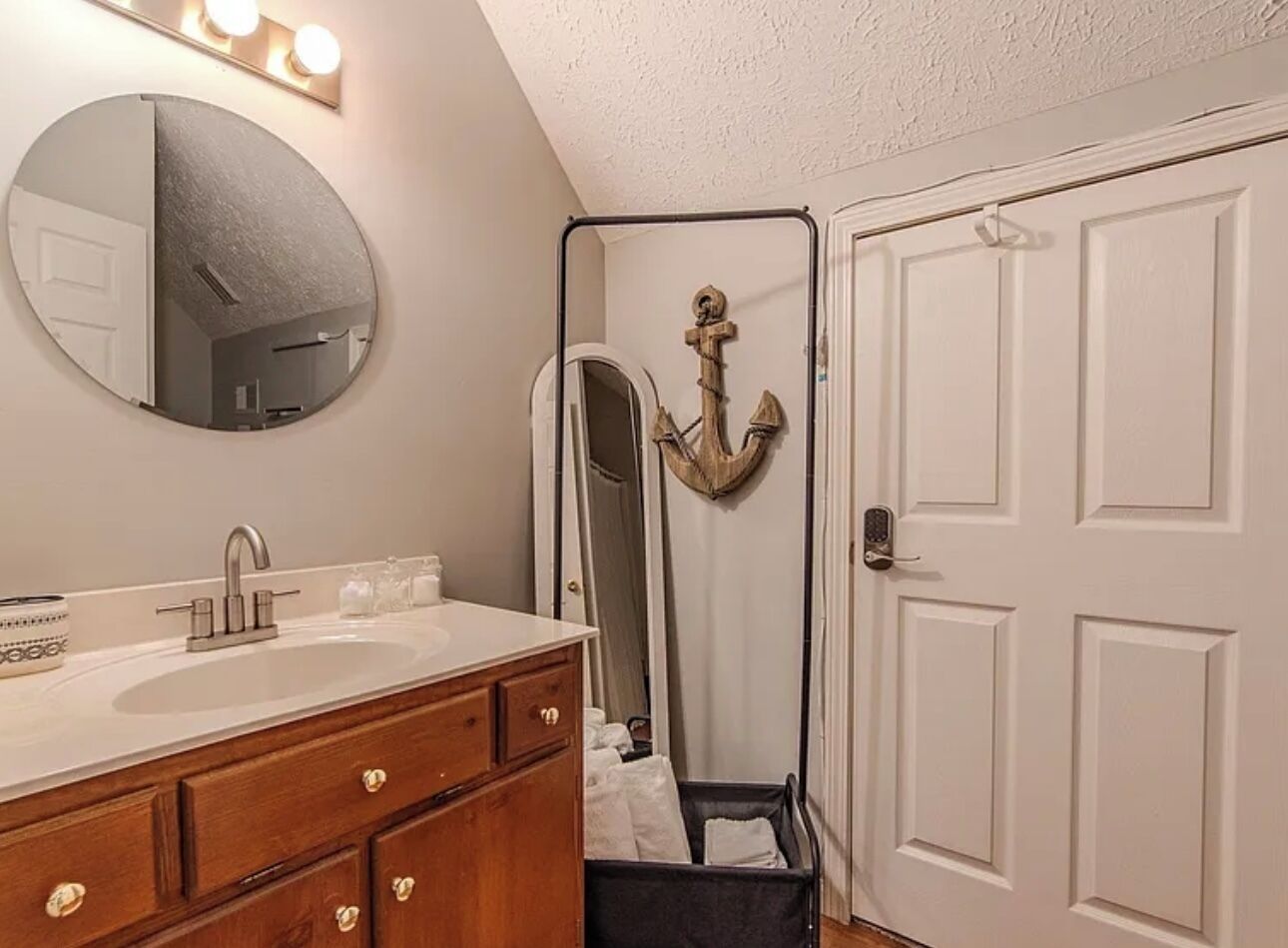 A bathroom with a round mirror, a sink, wooden cabinets, and a door with a coat rack.
