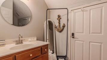 A bathroom with a round mirror, a sink, wooden cabinets, and a door with a coat rack.