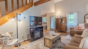 Amplia sala de estar con techo alto, vigas de madera, chimenea, televisor y un rincón de descanso acogedor.