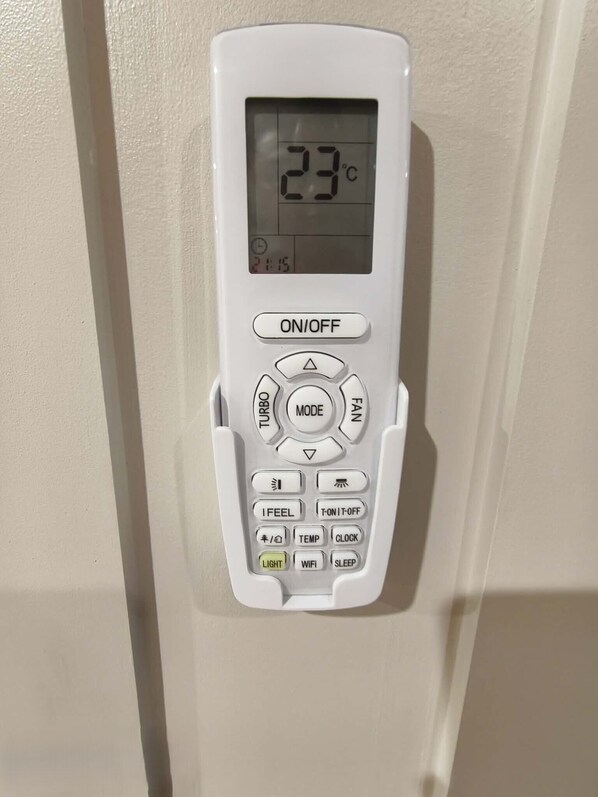 A thermostat with a digital display showing 23°C, ON/OFF button, mode selector, and various function buttons including LIGHT, TEMP, and CLOCK. - Natura Lagoon Bungalow 3 (Rarotonga)