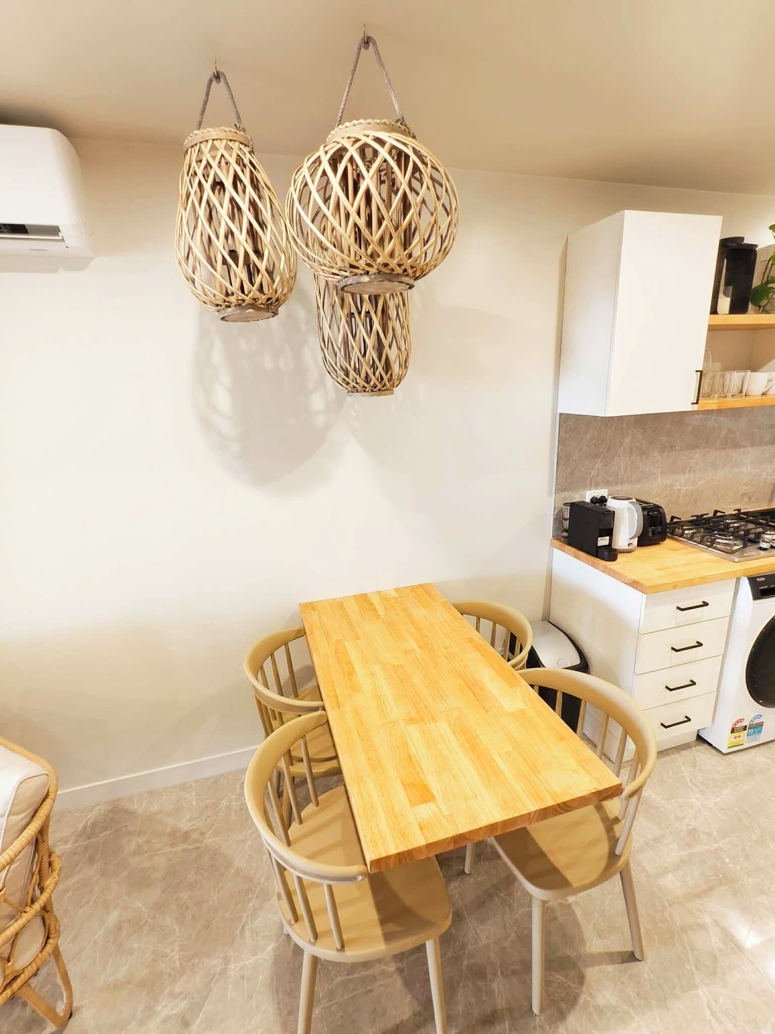 A modern kitchen with a wooden table and chairs, a gas stove, and two woven pendant lights.