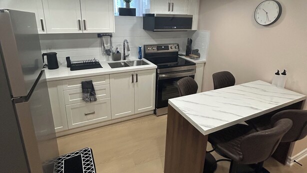 A modern kitchen with white cabinets, a built-in oven, a microwave, and a dining area with a marble table and four chairs. - 2 bedroom 1 bathroom basement apartment (Brampton)