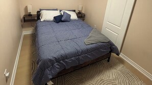 A bedroom with a bed, a nightstand, a lamp, a wall-mounted picture, a door, and a ceiling light. - 2 bedroom 1 bathroom basement apartment (Brampton)