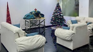Ett modernt vardagsrum med två vita lädersoffor, ett litet bord med en julgran, en kristallkrona och en röd julgransprydnad.