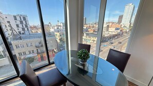 Una habitación moderna con una mesa y sillas de vidrio, una planta en maceta y vistas a la ciudad a través de amplios ventanales.
