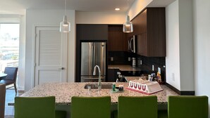 Una cocina moderna con encimeras de granito, electrodomésticos de acero inoxidable y sillas verdes.