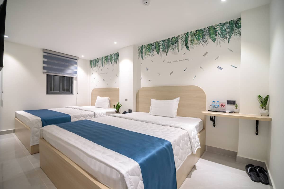 Une chambre d’hôtel avec deux lits, un petit bureau, une plante et un porte-chaussures.