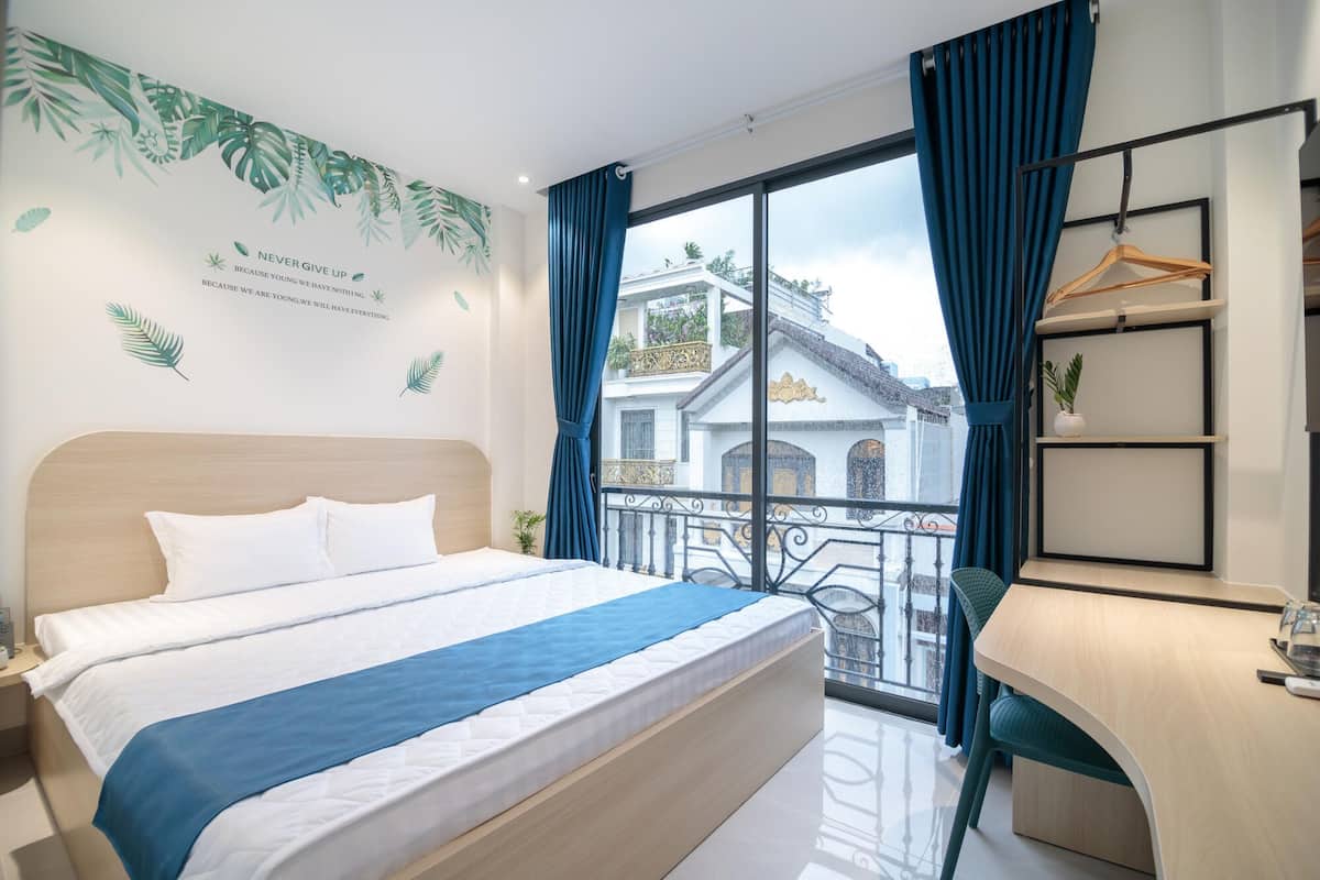 Une chambre d’hôtel avec un lit, un bureau et un balcon donnant sur un immeuble.