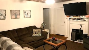 Ein Wohnzimmer mit braunem Sofa, Couchtisch, Flachbildfernseher und Kamin mit Kaminfeuer.