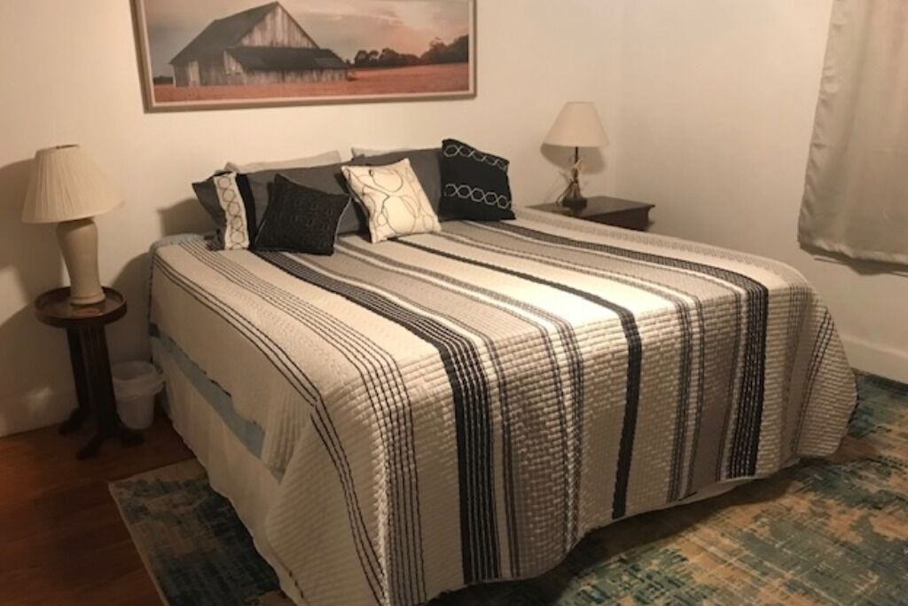 A bedroom with a bed, two bedside tables, a lamp, a rug, and a painting on the wall.