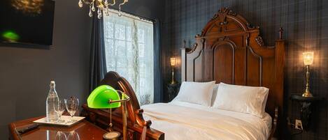 A bedroom with a wooden bed, a desk with a lamp, and a chandelier.