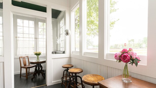 A room with a wooden table and two stools, a chair, and a vase with flowers. - The August Inn (Spring)