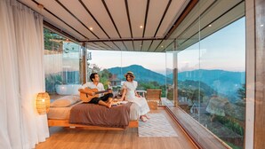 A bedroom with a large glass window, wooden flooring, and a bed with a view of the mountains. - Baan La Ong Fah 2-Mon Jam (Mae Rim)