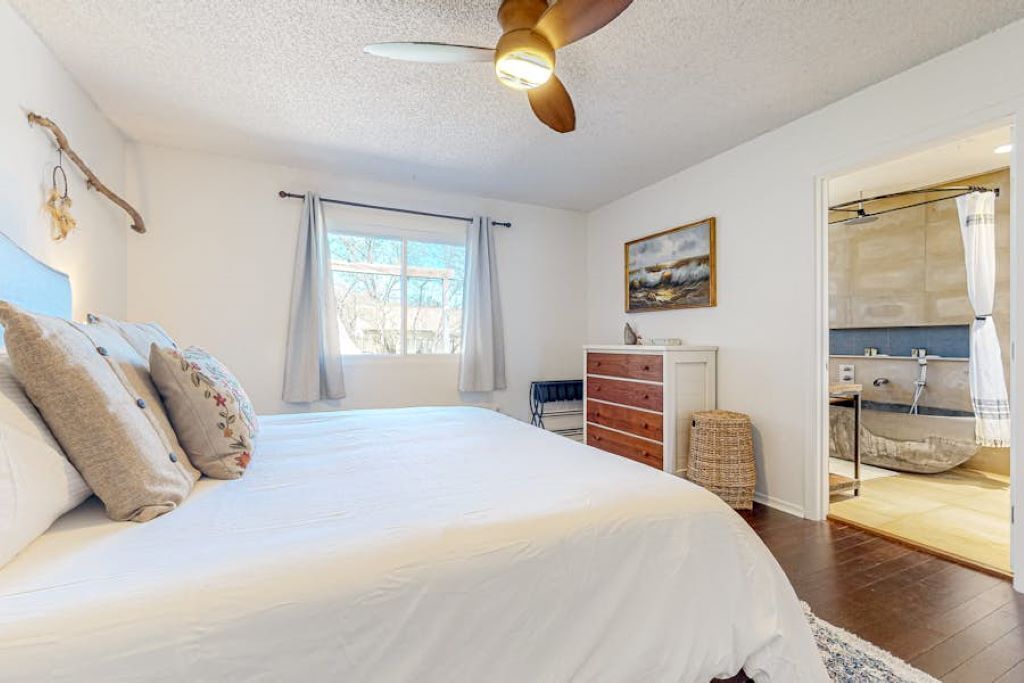 Une chambre à coucher comprenant un lit, un ventilateur de plafond, une commode, une fenêtre avec des rideaux et une salle de bain avec une douche.