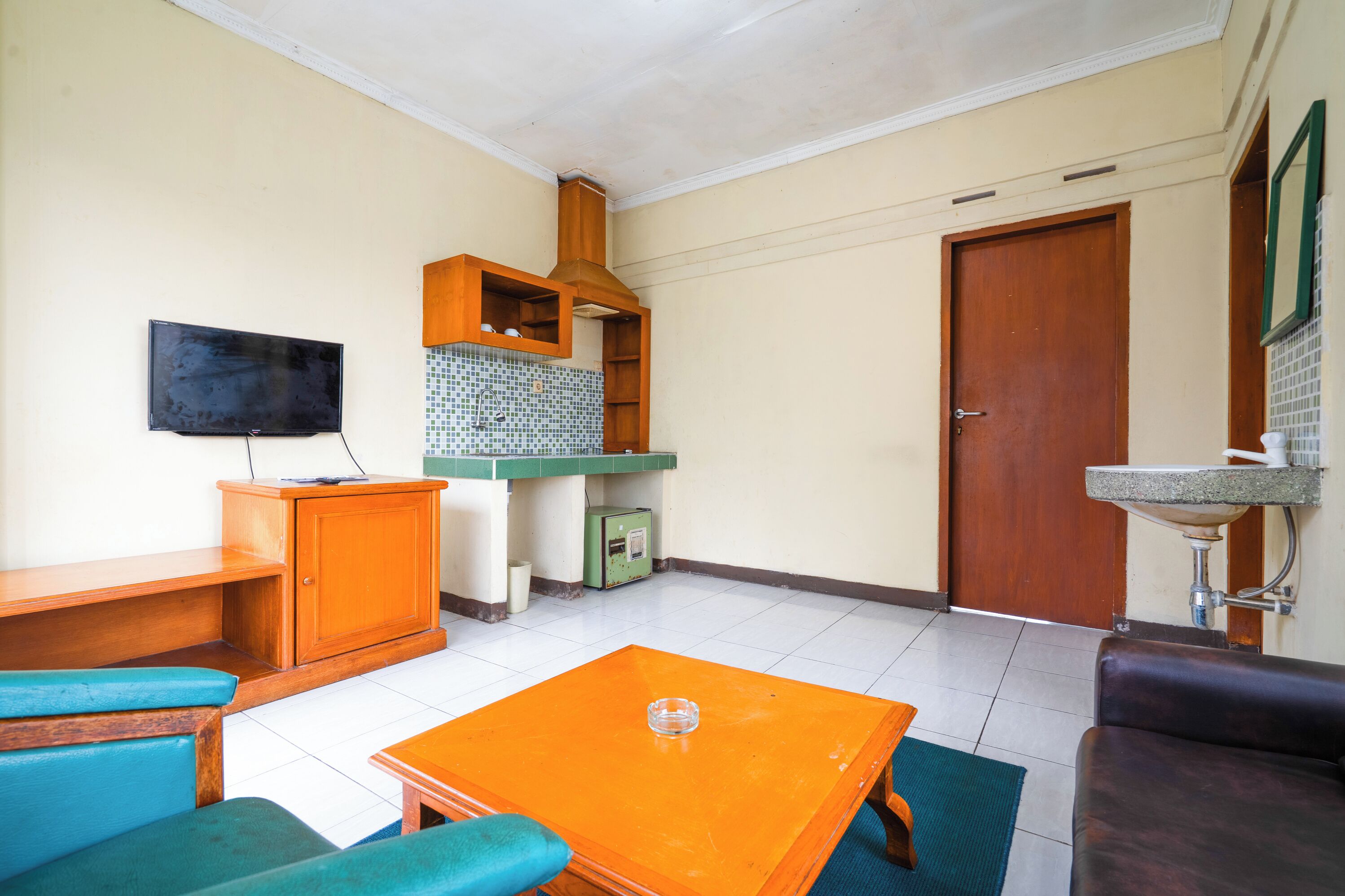 A small, compact living space with a kitchenette, a television, a wooden cabinet, a sofa, and a table.