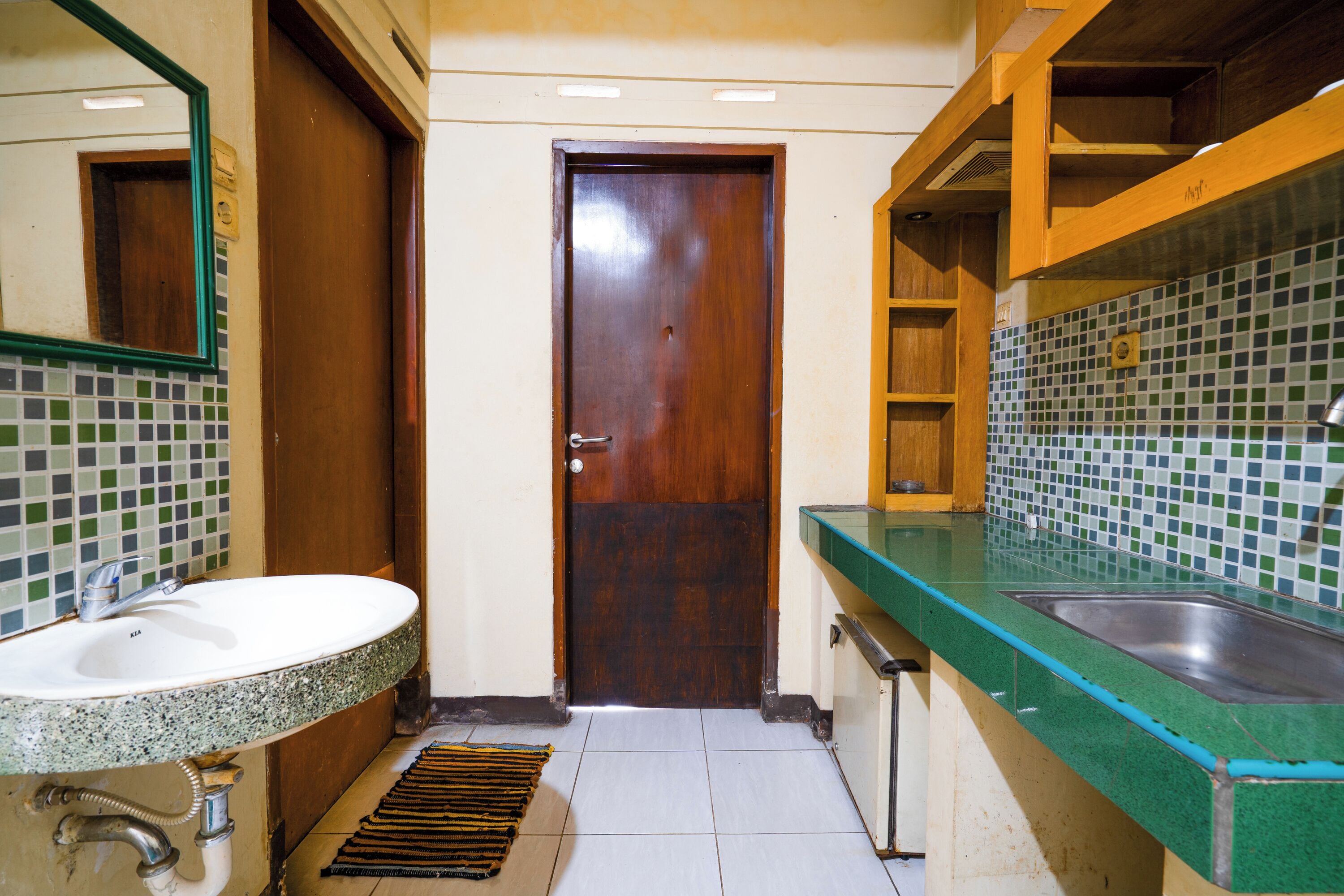 Un baño con puerta de madera, un lavamanos con encimera verde y un salpicadero de azulejos.