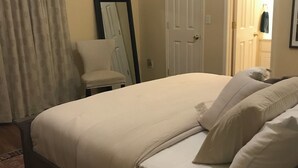 A neatly arranged bedroom with a large bed, a chair, and a door leading to another room.