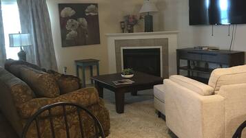 A living room with a fireplace, a ceiling fan, a TV, and a dining table.
