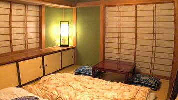 Habitació japonesa tradicional amb sòl de tatami, un llit de fusta baix amb mantell i estampat floral, una taula de fusta petita i una porta corredissa de shoji.