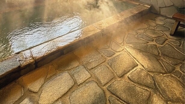 Sauna con suelo de piedra, banco de piedra, paredes de madera y vistas a árboles a través de amplios ventanales.