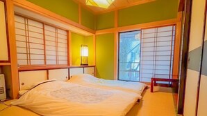 Una habitación tradicional japonesa con tatamis, una cama con ropa de cama blanca, puertas correderas y una lámpara colgante.