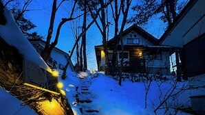 Un sendero cubierto de nieve que lleva a una casa con un porche visible y un letrero que dice 'TO THE HIDEOUT THIS WAY'.