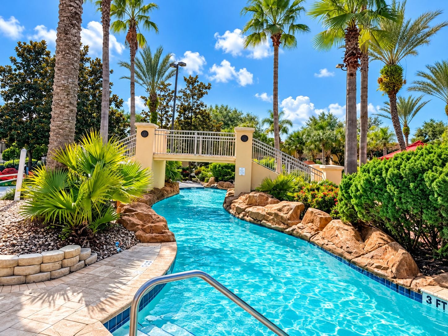 A swimming pool with a bridge, surrounded by palm trees and rocks.
