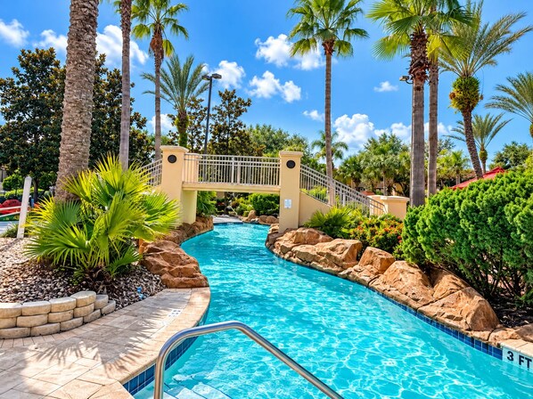 A swimming pool with a bridge, surrounded by palm trees and rocks.