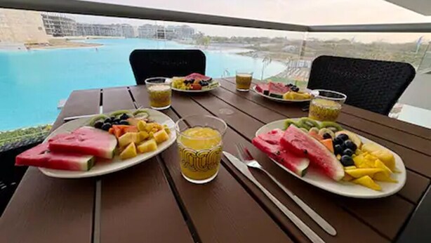 A table with plates of fruit and a glass of juice, overlooking a body of water. - Cartagena Baia Kristal | Perfect Escape Kabo 1-Apt 2 F (Cartagena de Indias)
