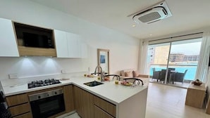 A modern kitchen with a central island, a built-in oven, and a large window overlooking a balcony. - Cartagena Baia Kristal | Perfect Escape Kabo 1-Apt 2 F (Cartagena de Indias)