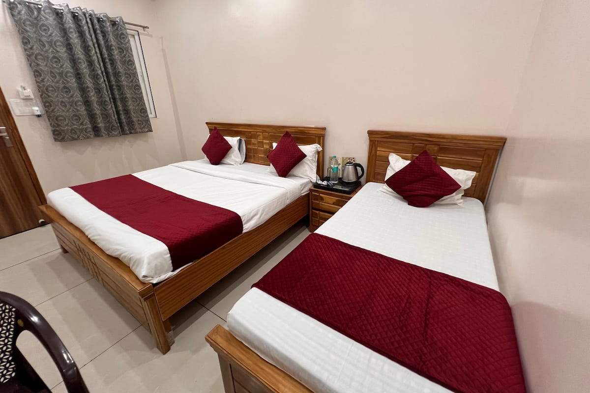 A hotel room with two wooden beds, each with white and red bedding, a wooden nightstand, and a grey patterned curtain.