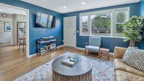Un salon avec un mur bleu, un parquet, une table basse ronde, un canapé, un téléviseur et une bibliothèque.