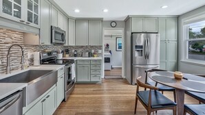 Une cuisine moderne dotée d’appareils électroménagers en acier inoxydable, de meubles de couleur vert clair et d’une table à manger en bois avec des chaises.