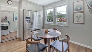 Une cuisine moderne équipée d’un réfrigérateur en acier inoxydable, d’une table à manger avec quatre chaises et d’une fenêtre donnant sur l’extérieur.