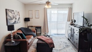 A living room with a sofa, ottoman, TV, and a ceiling fan. - Steps from Shands. Ready for Rotations: Mid-July and October Rotations Available (Gainesville)