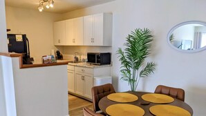 A compact kitchen with white cabinets, a microwave, and a sink. There is a dining table with four chairs and a potted plant. - Steps from Shands. Ready for Rotations: Mid-July and October Rotations Available (Gainesville)
