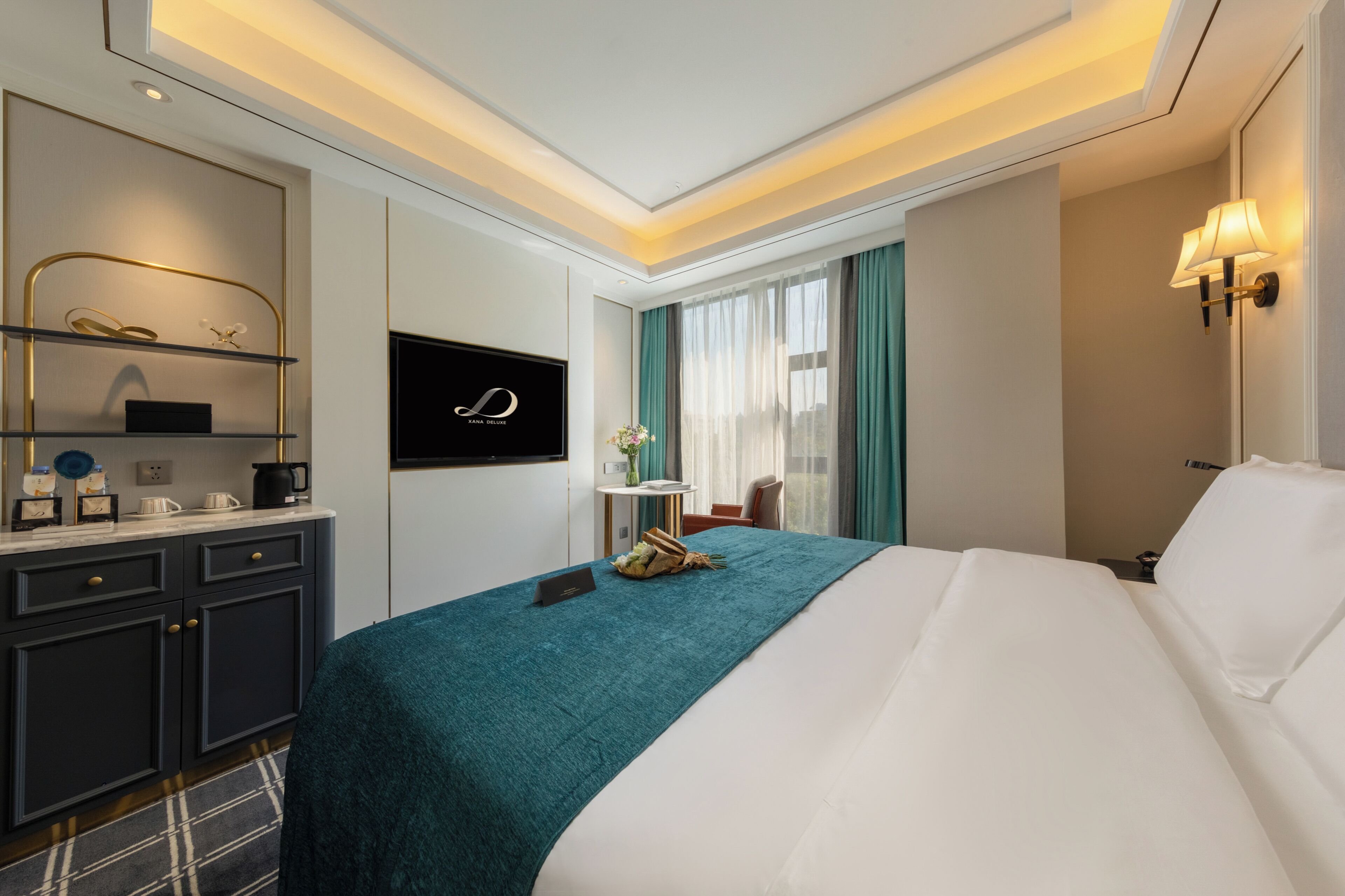 A modern hotel room with a large bed, a desk with a laptop, a flat-screen TV, and a small table with a vase.