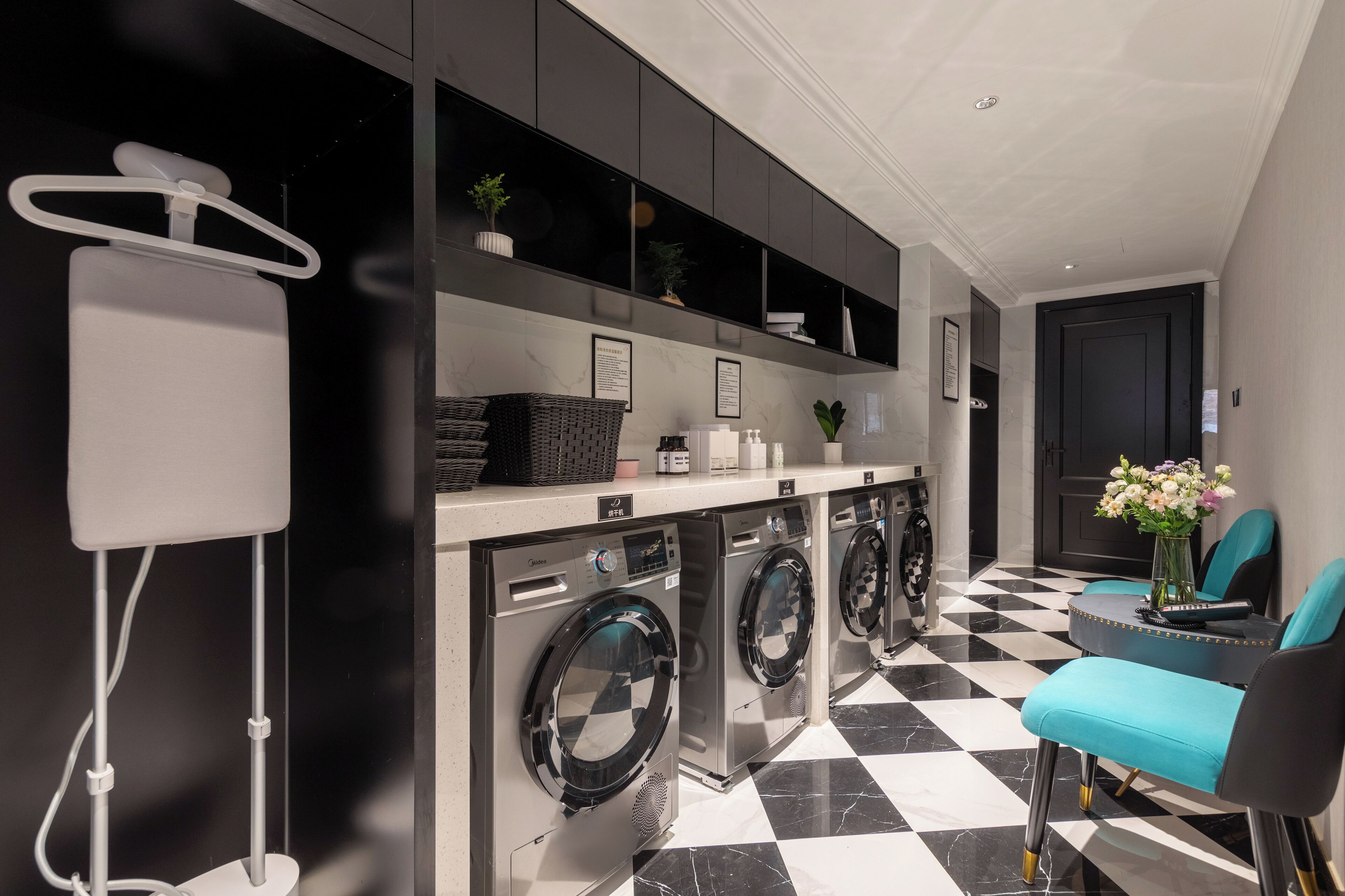 A modern laundry area with a checkered floor, a washing machine, a drying rack, and a small table with chairs.