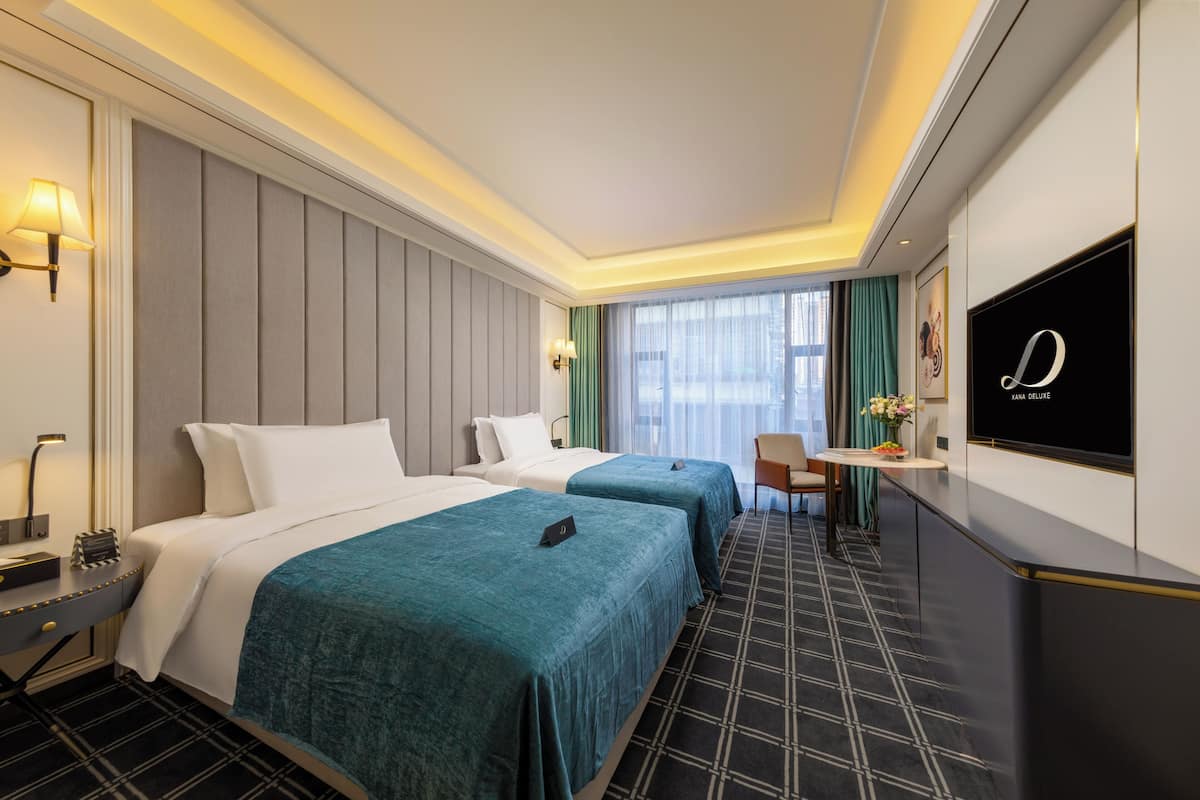 A hotel room with two beds, a desk, a chair, a TV, and a window with curtains.