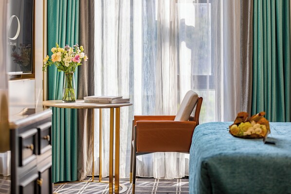 A hotel room with a bed, a chair, a table with a vase of flowers, and curtains. - XANA Deluxe International Hotel Dongshankou Metro Station Branch (Guangzhou)