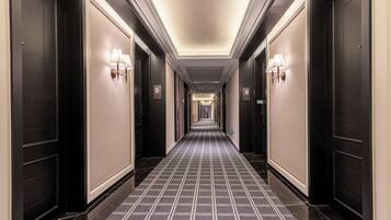 A long, narrow hotel corridor with dark doors on either side, light wall sconces, and a checkered floor pattern.