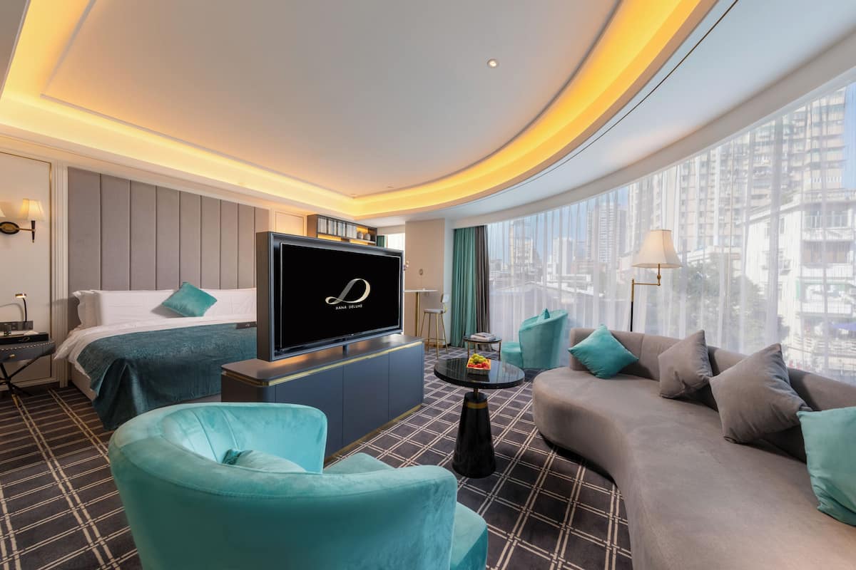 A modern hotel room with a large bed, a sofa, a TV, and a city view.