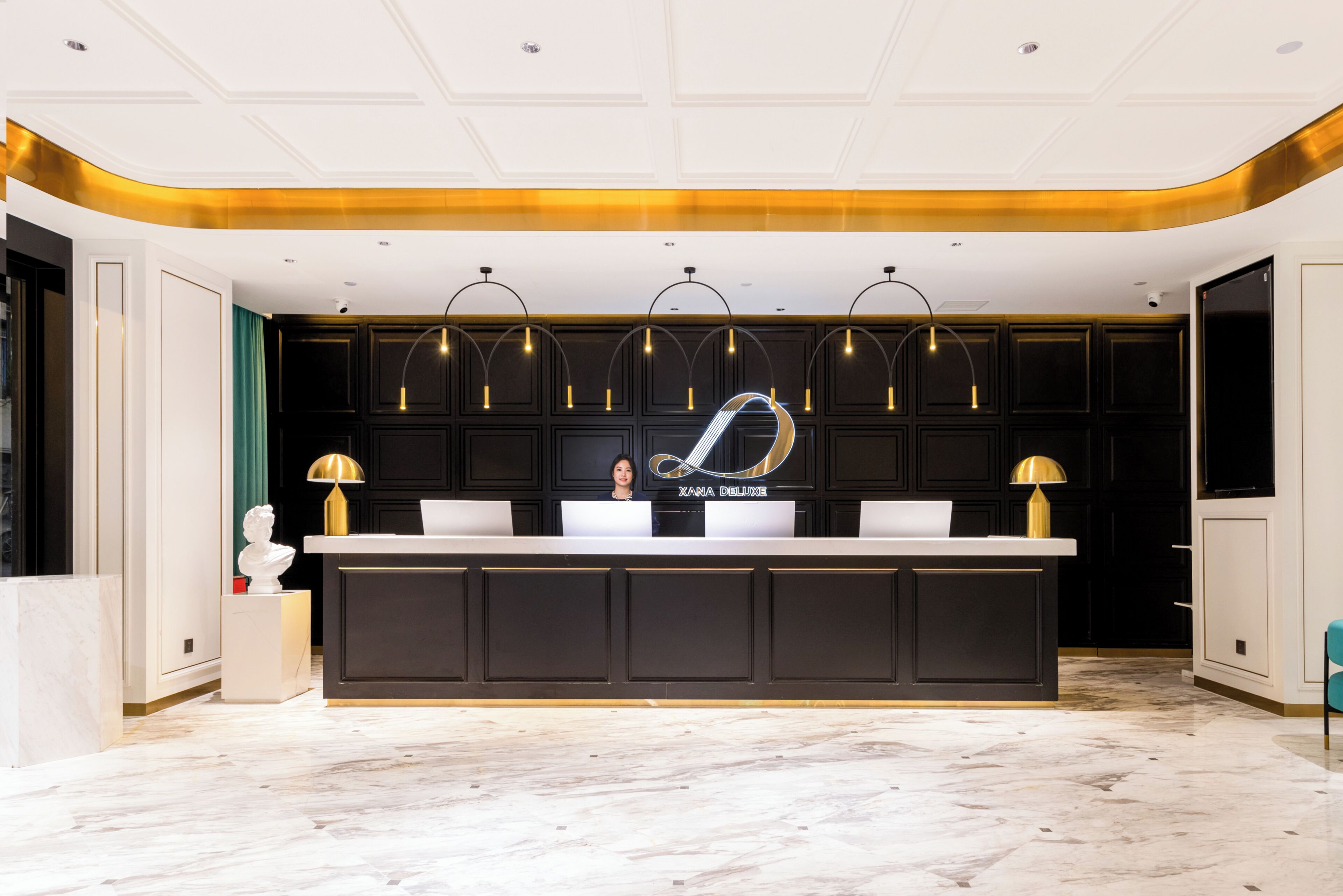 A reception desk with a modern design, featuring a large logo and multiple pendant lights.