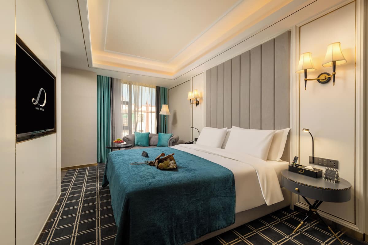 A hotel room with a bed, a bedside table, a TV, and a window with curtains.